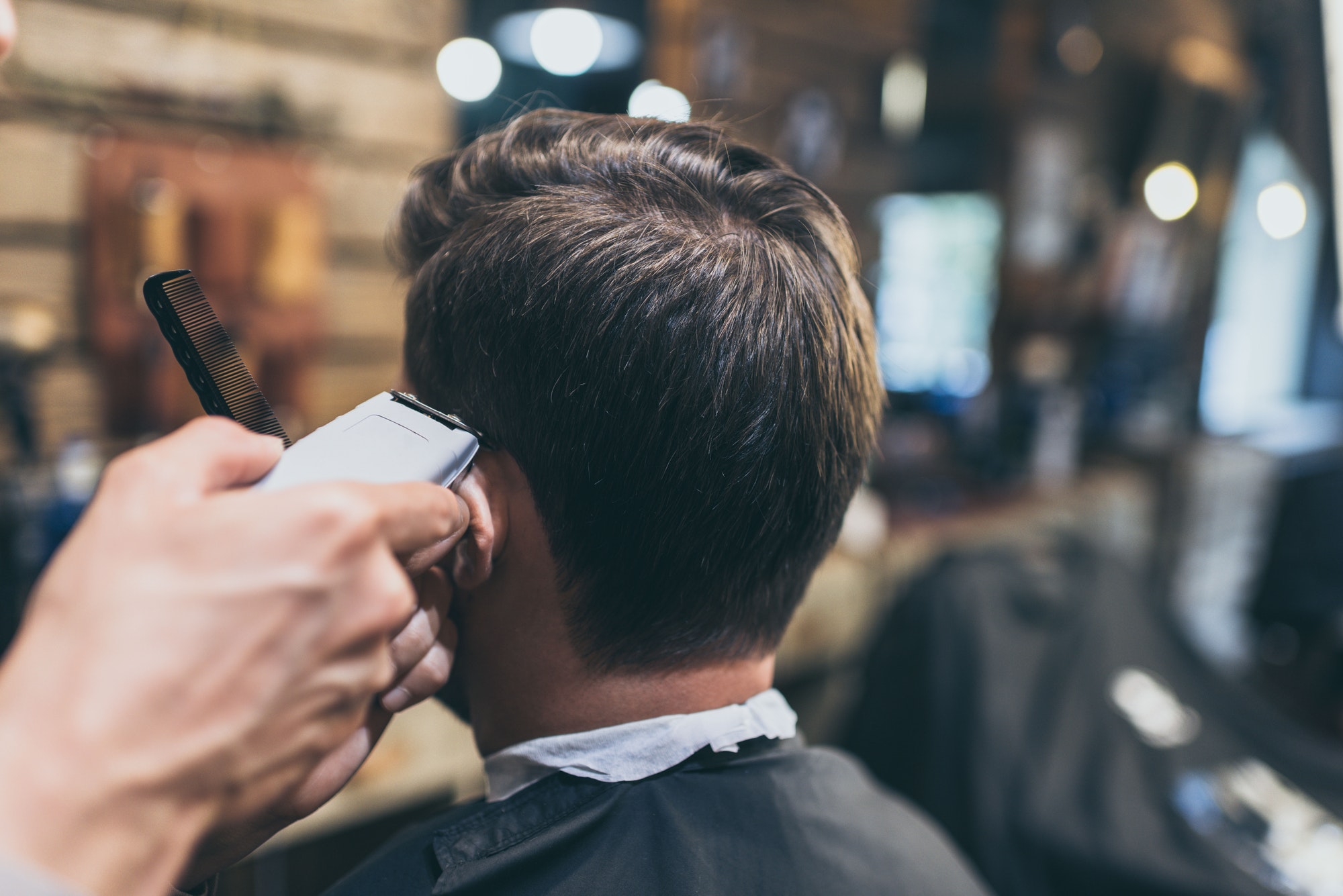 Male barber cutting hair of customer in barber shop